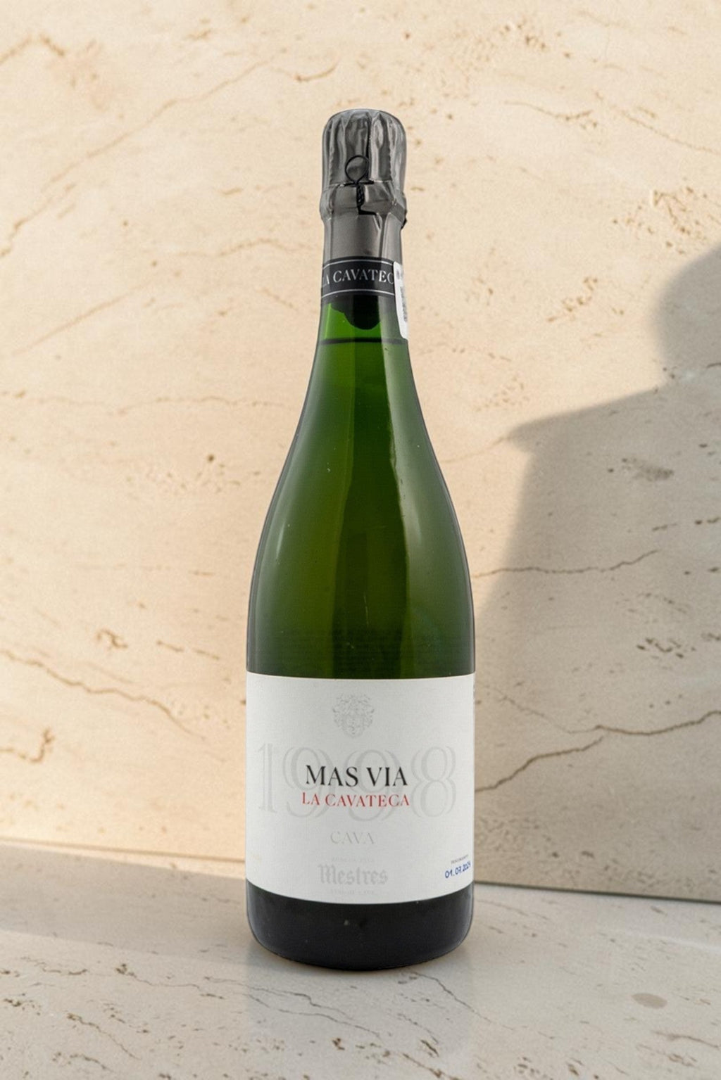 Botella de cava Mestres Cavateca MAS VIA 1998 de Wellnex sobre superficie de piedra clara