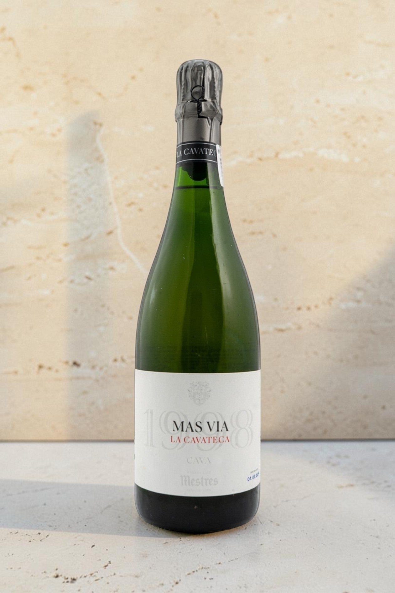 Botella de cava Wellnex Mestres Cavateca MAS VIA 1998 con etiqueta elegante sobre superficie de piedra clara