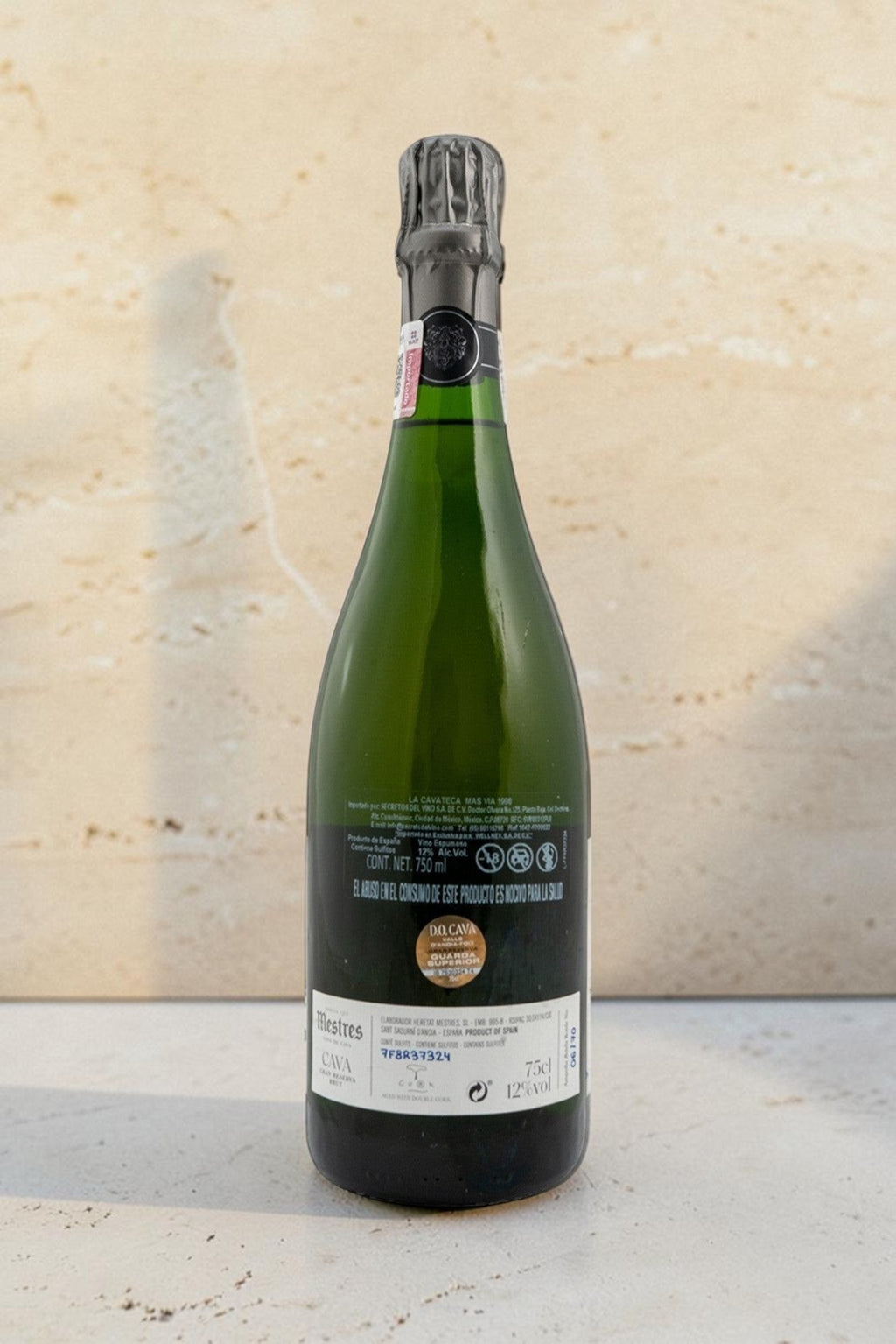 Botella de cava Mestres Cavateca MAS VIA 1998 de Wellnex, vista trasera con etiqueta detallada sobre fondo beige.