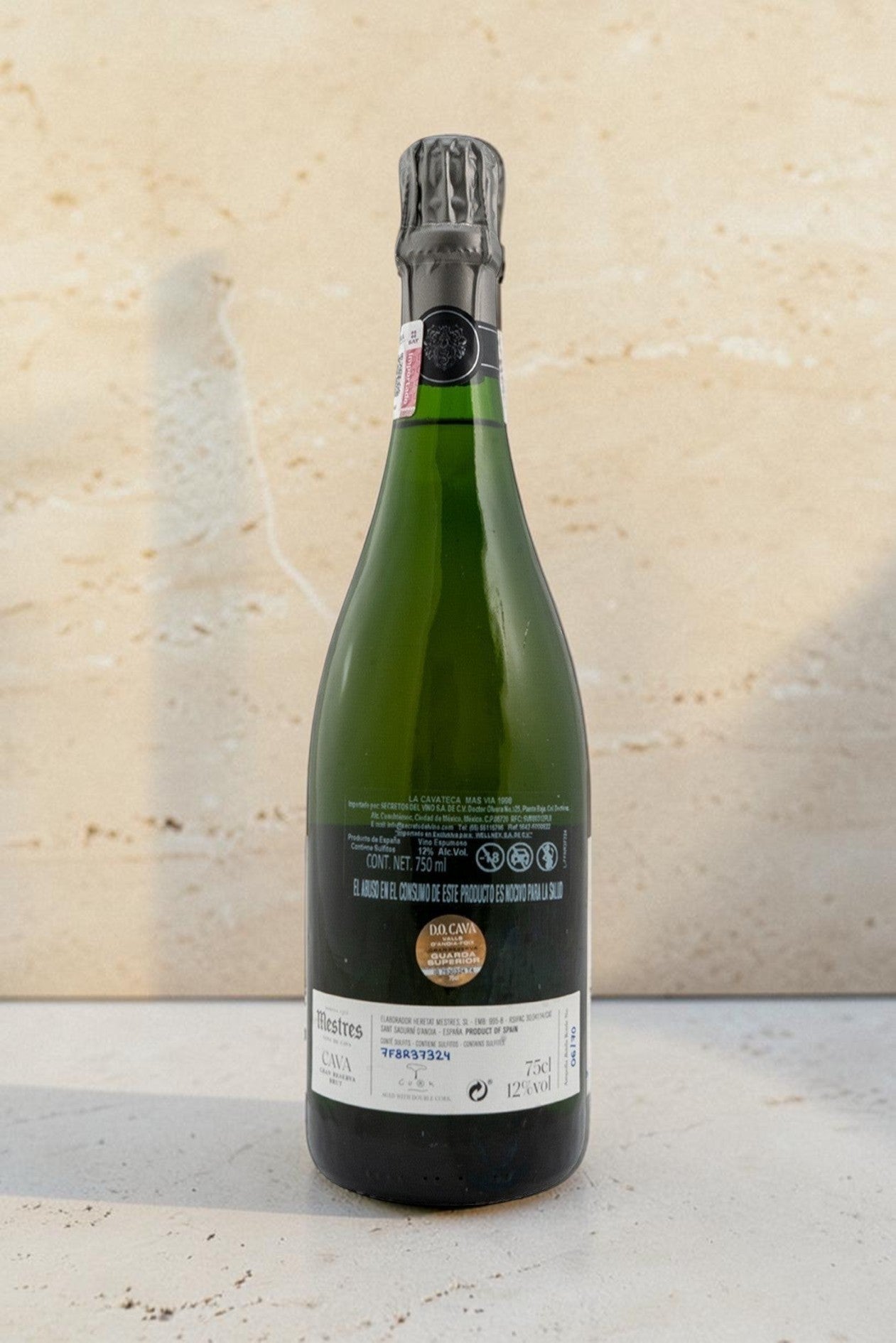 Botella de cava Mestres Cavateca MAS VIA 1998 de Wellnex, vista trasera con etiqueta detallada sobre fondo beige.