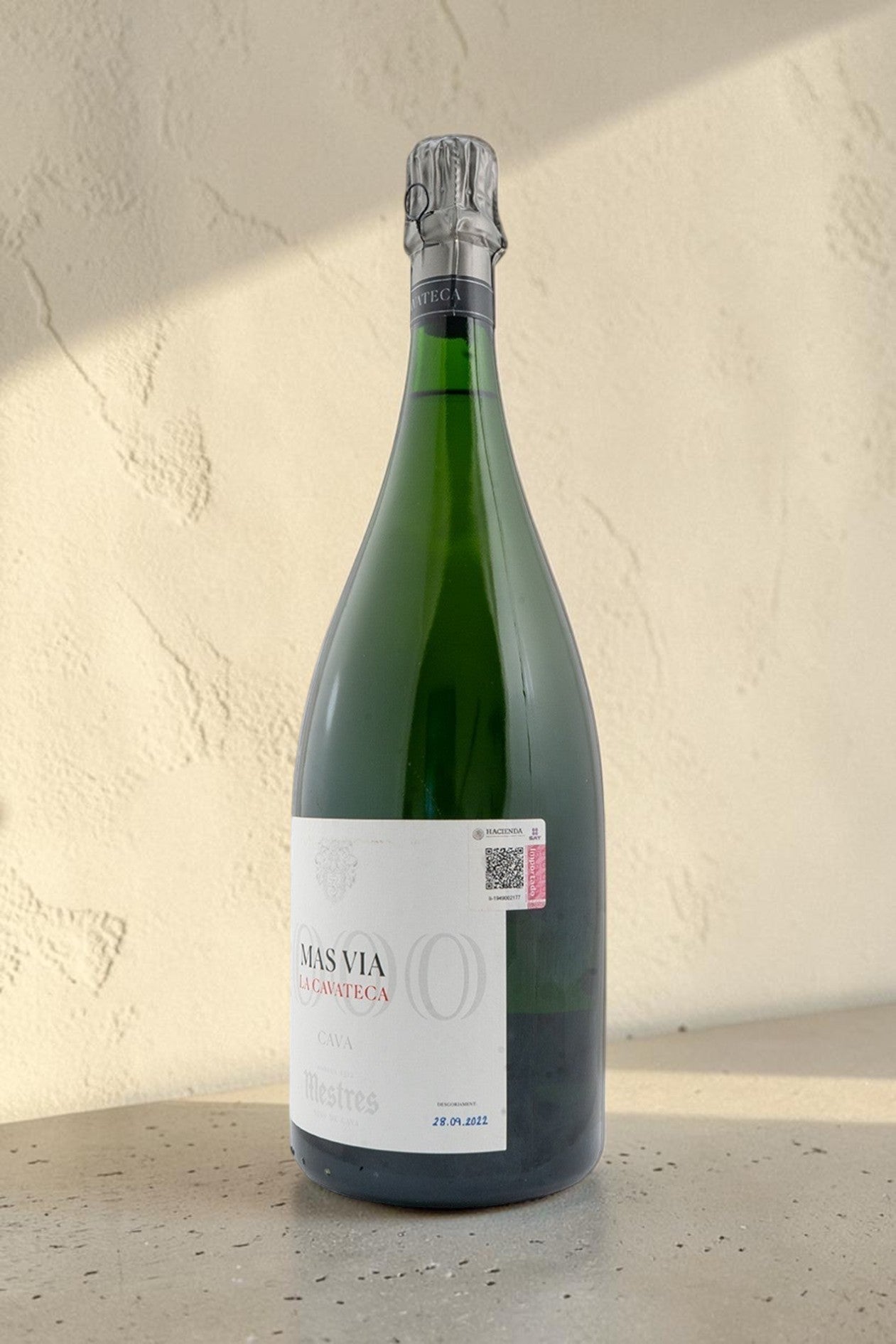 Botella Magnum de cava Mestres Cavateca 2000 Mas Via sobre fondo neutro con etiqueta elegante y cristal verde oscuro