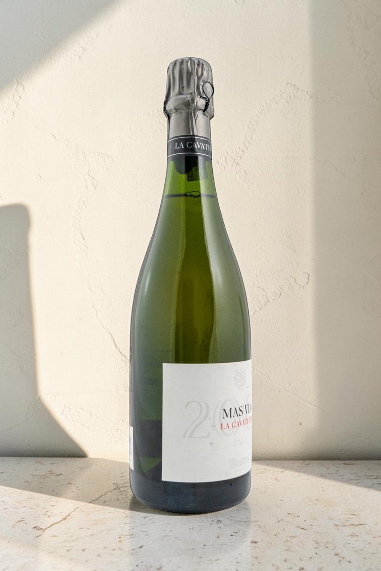 Botella de cava Mestres Cavateca MAS VIA 2002 de Wellnex sobre superficie de piedra con iluminación natural