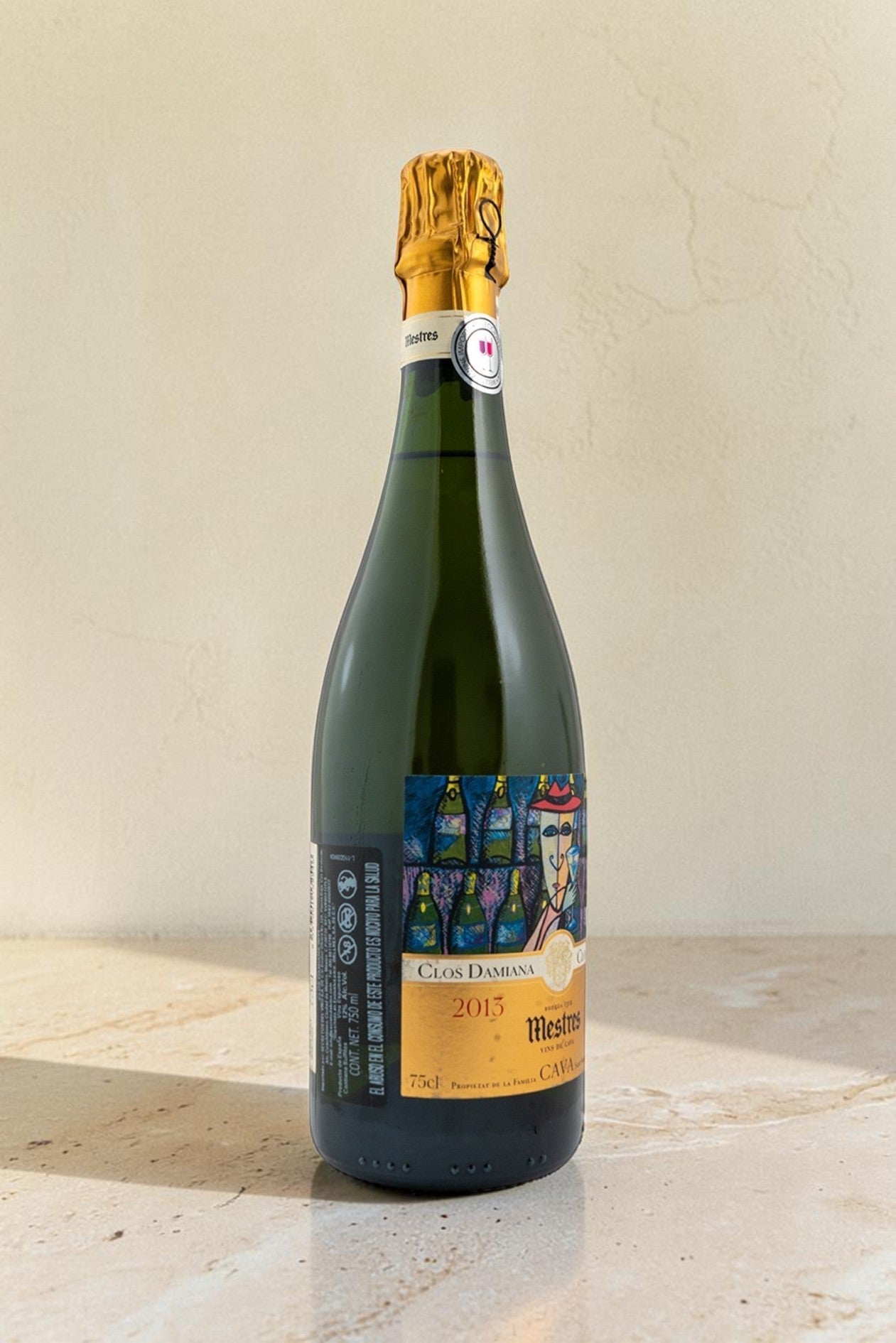 Botella de cava Wellnex Mestres Clos Damiana 2015 con etiqueta artística sobre superficie de piedra clara