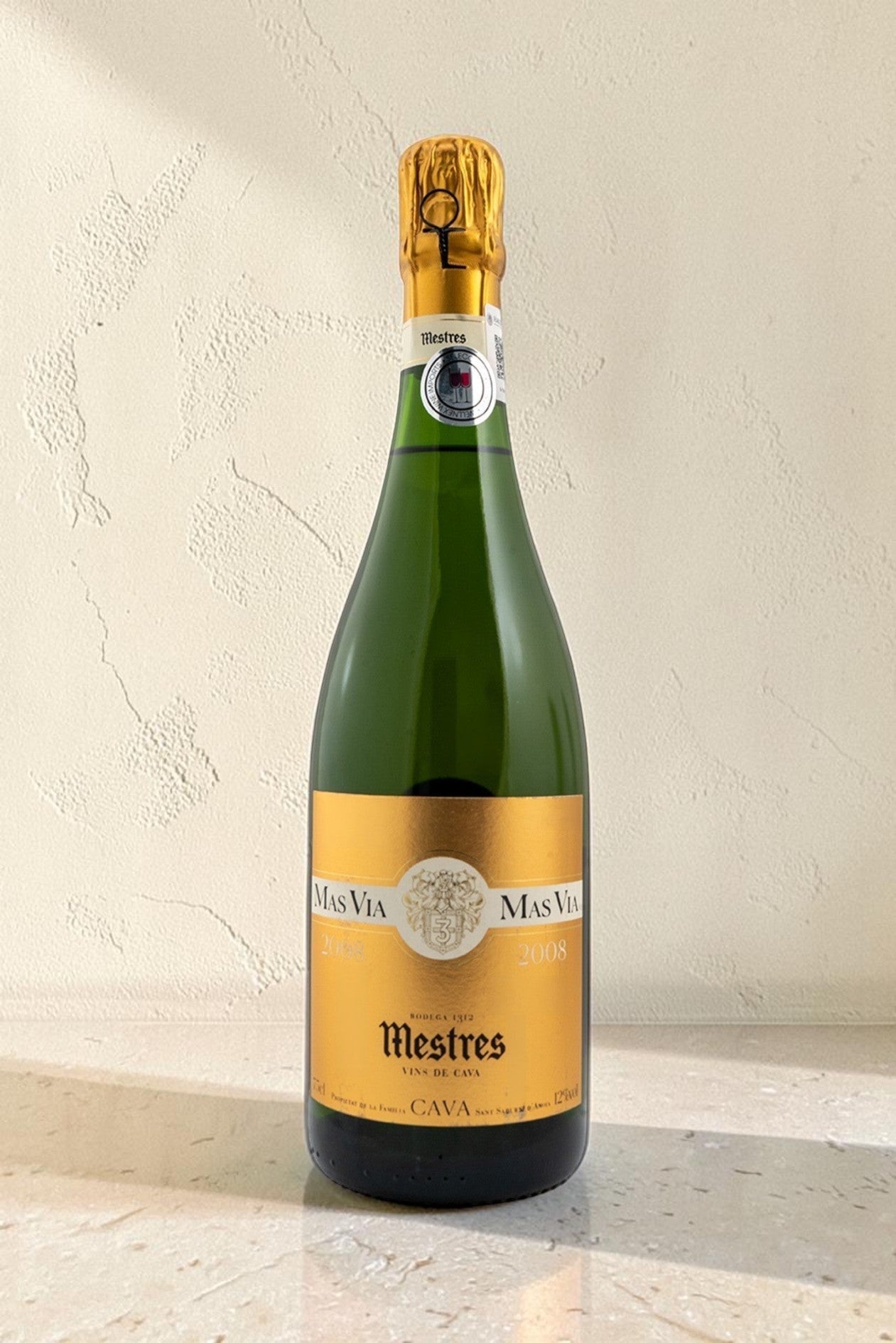 Botella de cava Wellnex Mestres MAS VIA 2008 con etiqueta dorada sobre fondo neutro