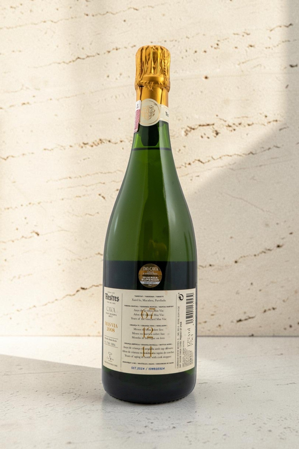 Botella de cava Mestres MAS VIA de Wellnex con etiqueta detallada y cápsula dorada sobre fondo de piedra natural