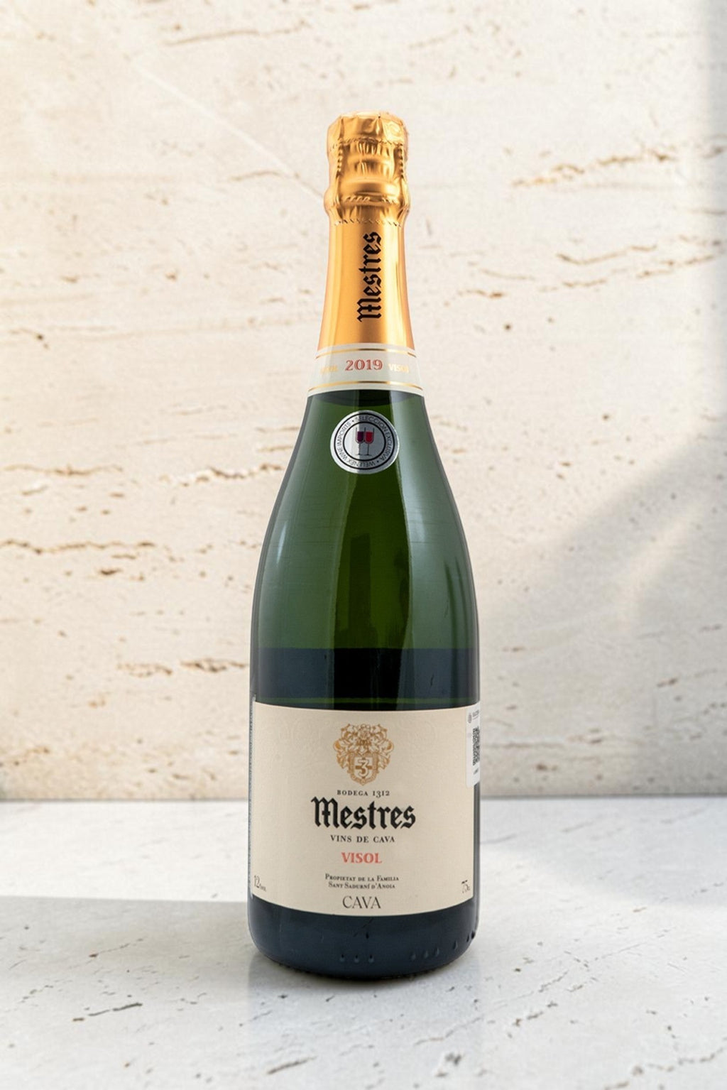 Botella de cava Wellnex Mestres Visol 2019 con etiqueta elegante y cápsula dorada sobre fondo de piedra clara
