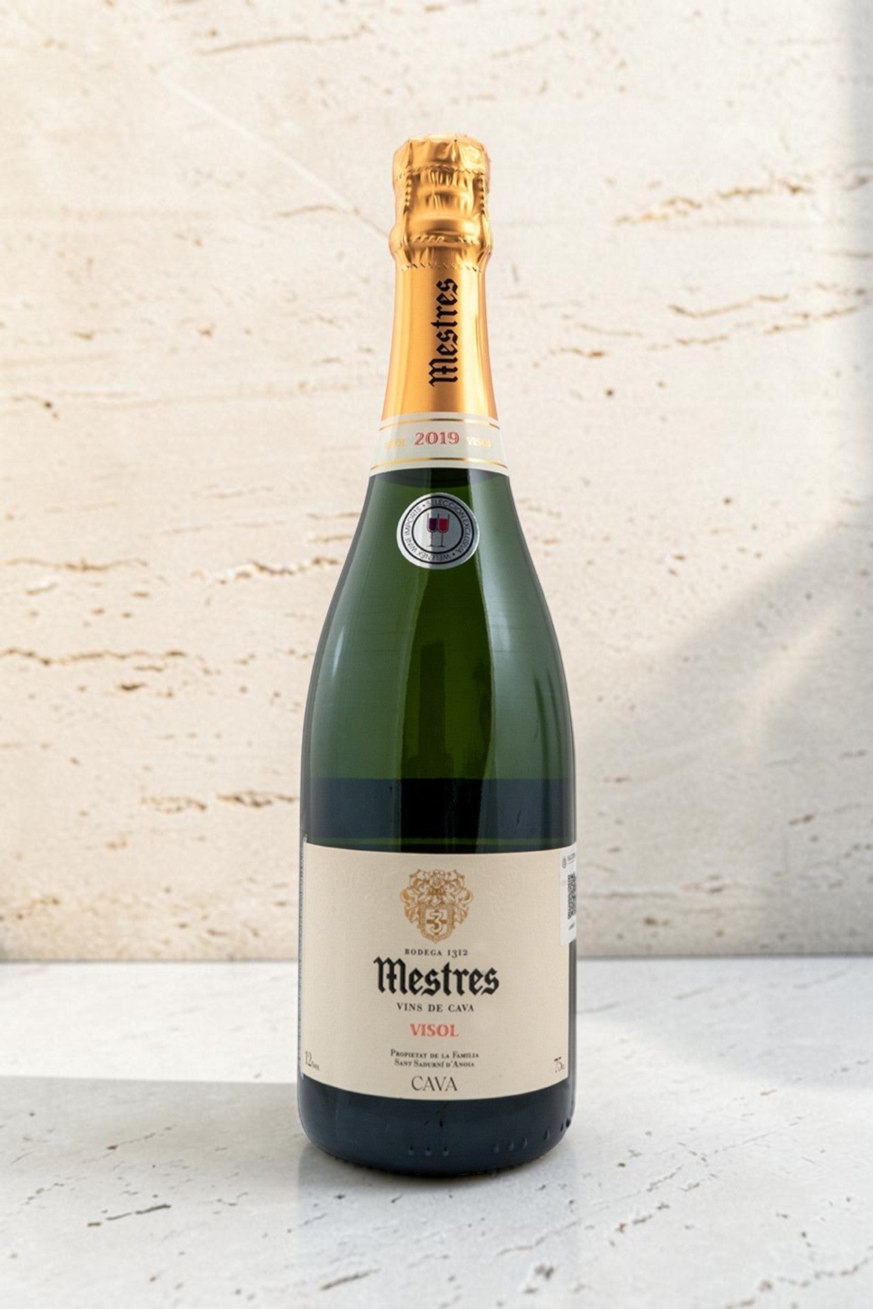 Botella de cava Wellnex Mestres Visol 2019 con etiqueta elegante y cápsula dorada sobre fondo de piedra clara
