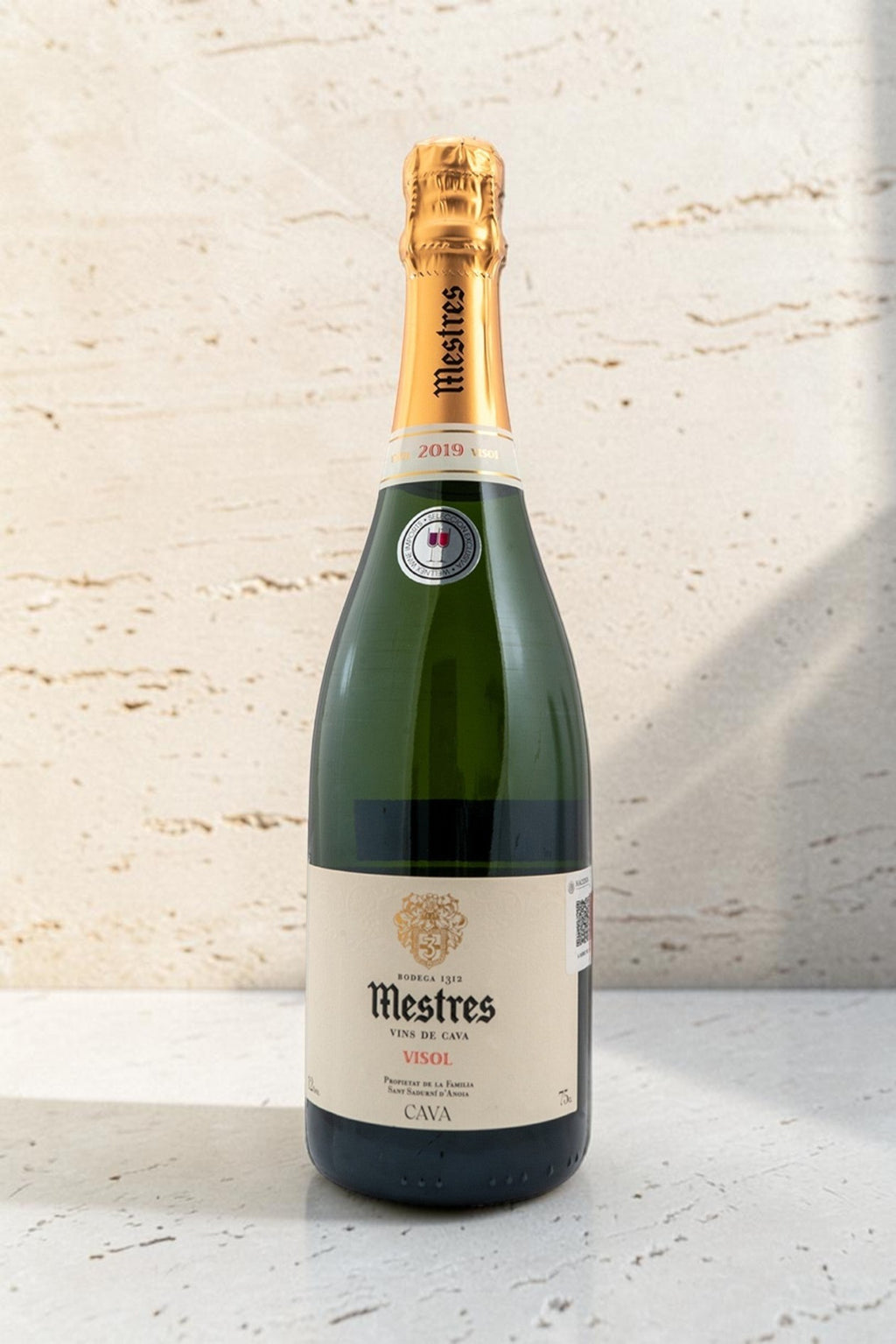 Botella de cava Wellnex Mestres Visol 2019 con etiqueta elegante y cápsula dorada sobre fondo de piedra natural