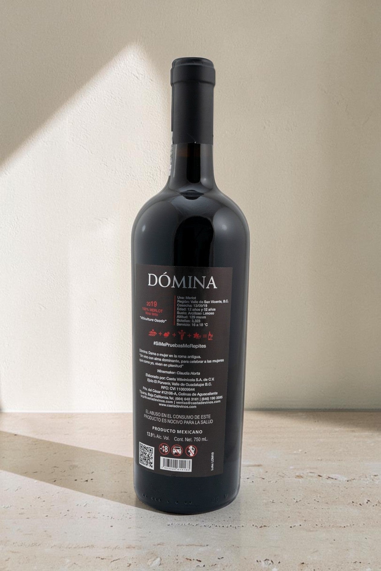 Botella de vino tinto Wellnex Domina Magnum, Merlot mexicano con etiqueta informativa sobre fondo neutro.