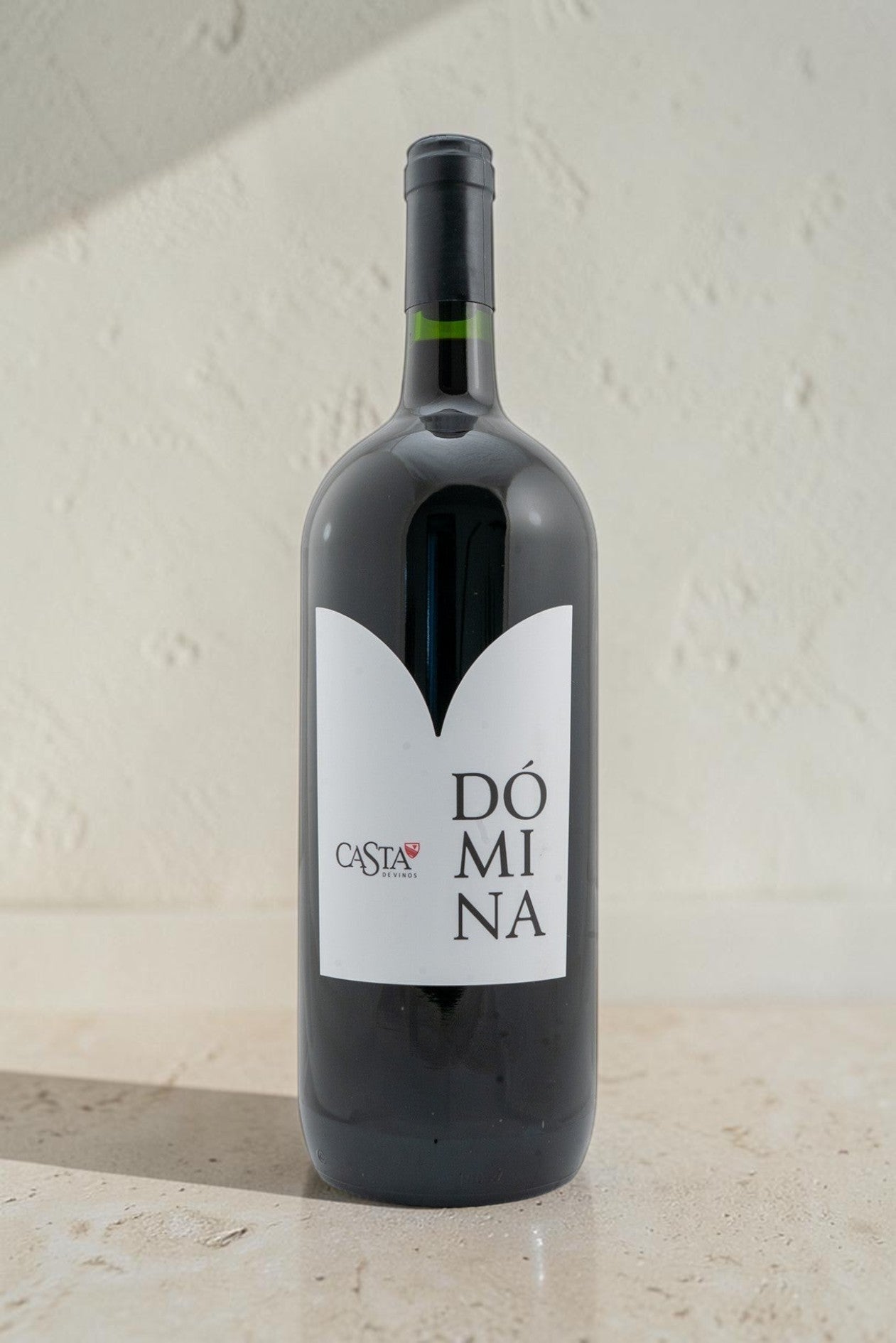 Botella de vino tinto Domina de Wellnex, color rojo rubí, con etiqueta minimalista sobre fondo claro.