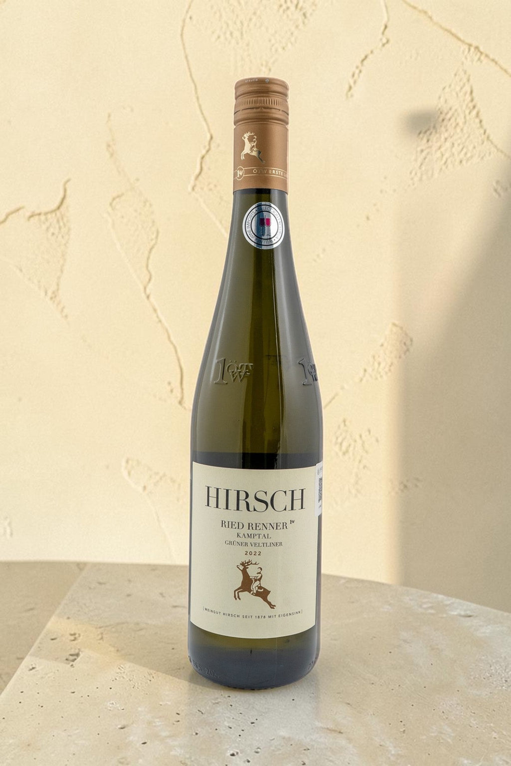 Botella de vino blanco Hirsch VB Ried Renner Kampler Gruner Veltliner de Wellnex sobre una mesa de piedra clara