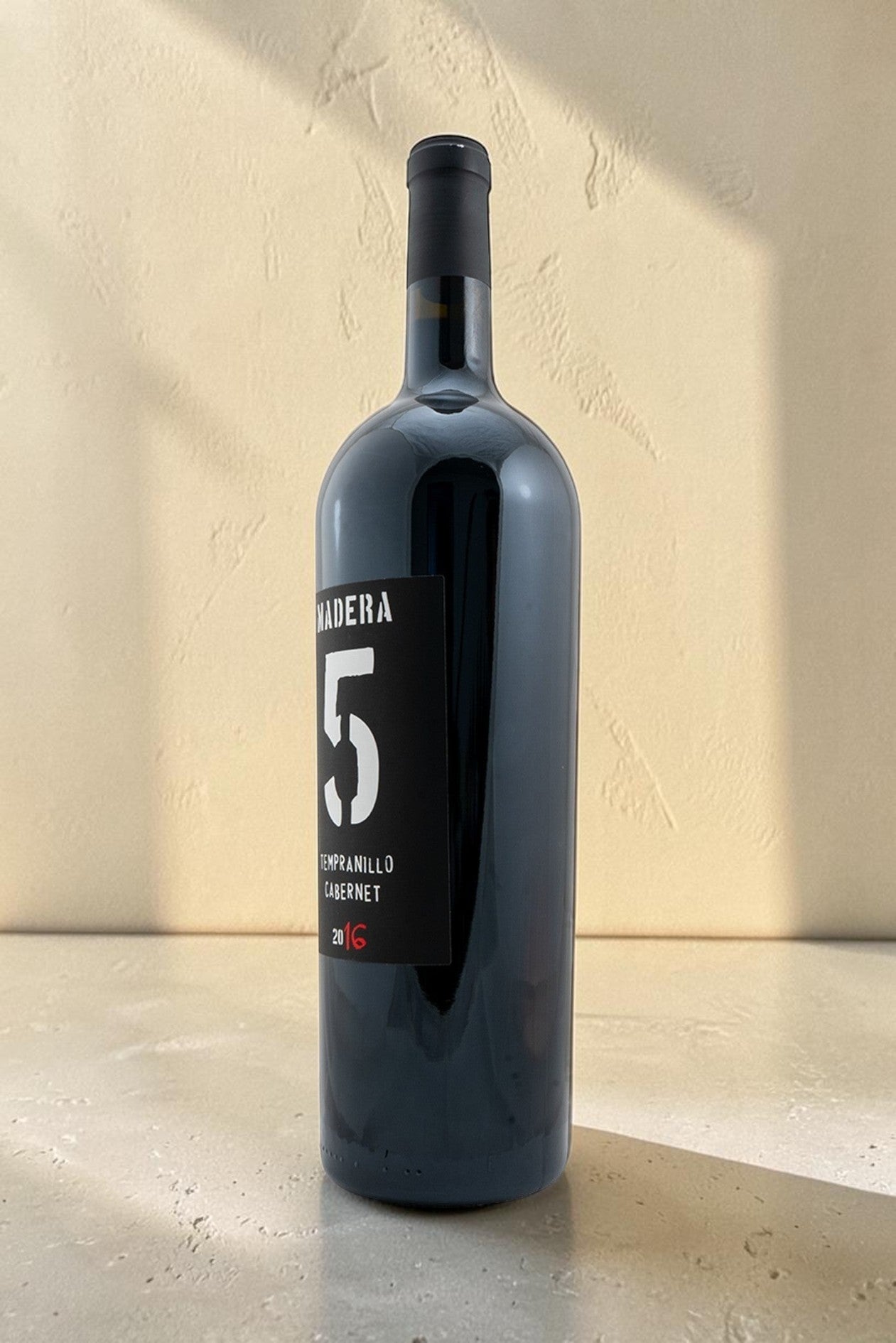 Botella de vino tinto Magnum Tempranillo Cabernet de Wellnex con etiqueta negra sobre fondo beige iluminado