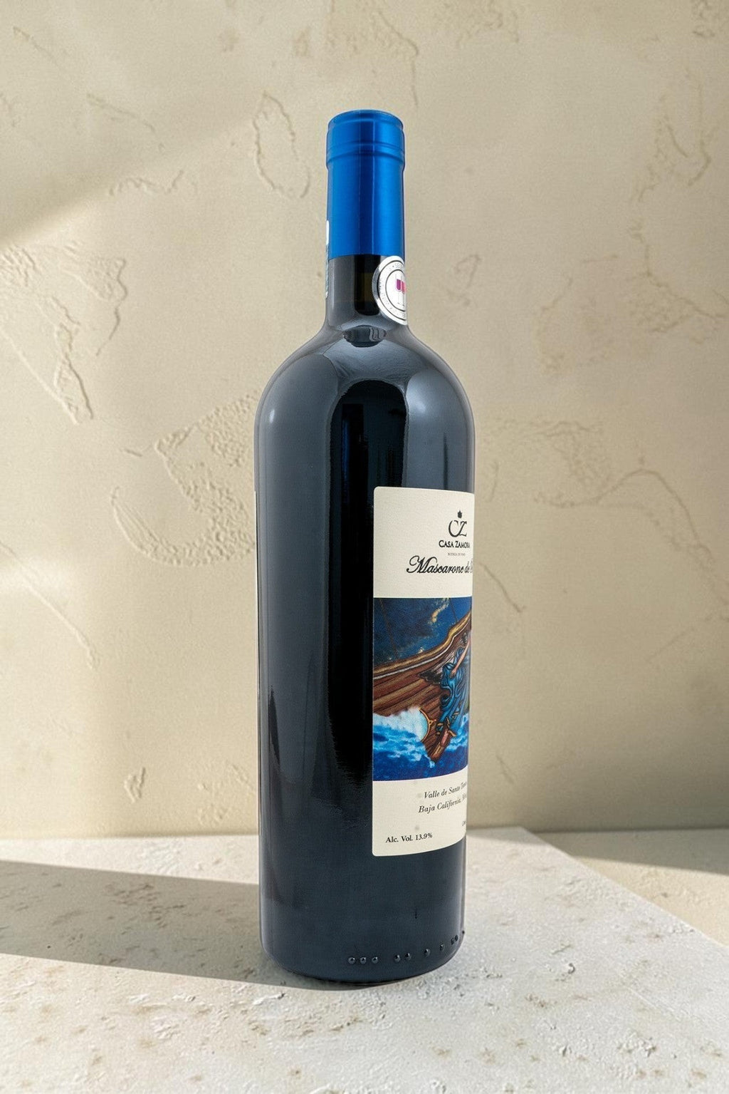 Botella de vino tinto Mascarone de Proa de Wellnex con etiqueta ilustrada y cápsula azul sobre fondo neutro