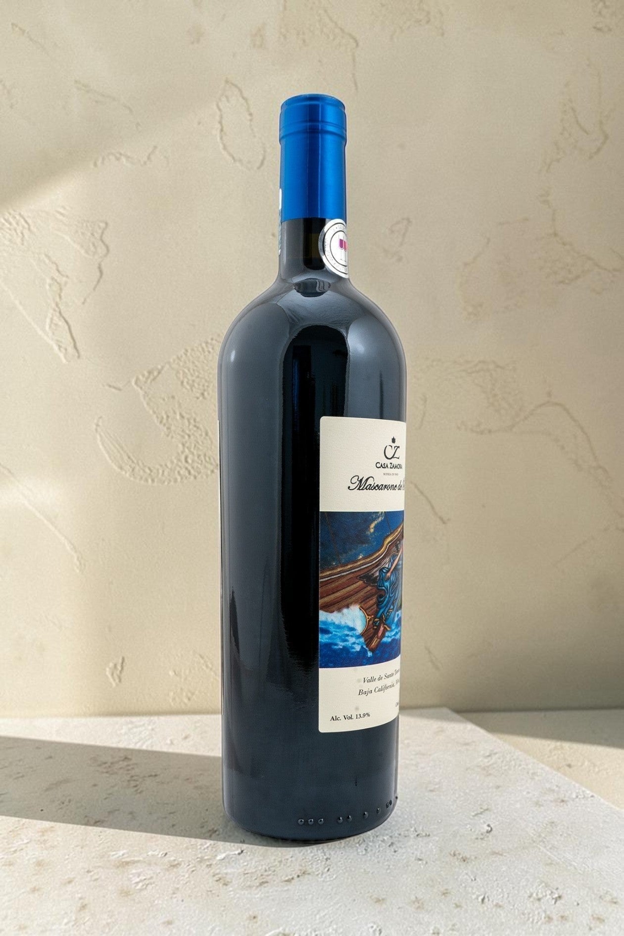 Botella de vino tinto Mascarone de Proa de Wellnex con etiqueta ilustrada y cápsula azul sobre fondo neutro