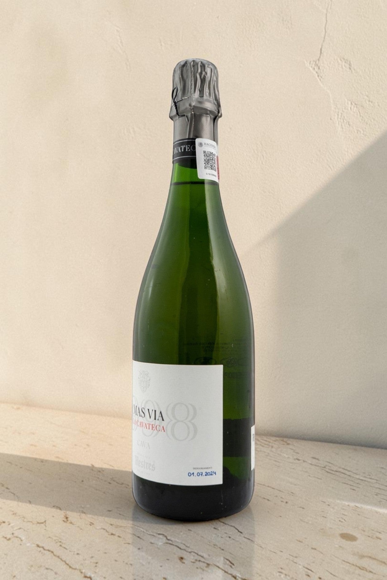 Botella de cava Wellnex Mestres Cavateca MAS VIA 1998 de cristal verde sobre superficie de piedra clara