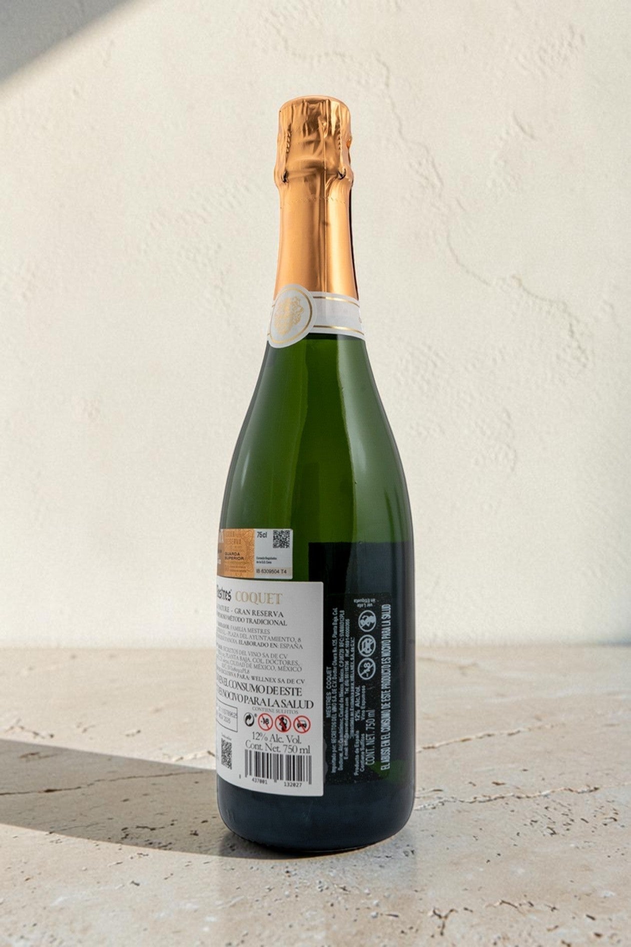 Botella de cava Wellnex Mestres Coquet con etiqueta trasera detallada sobre fondo de piedra clara