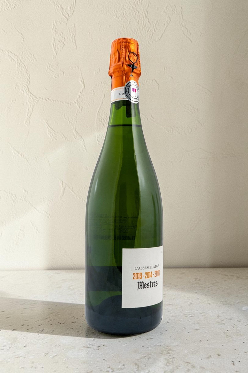 Botella de cava Wellnex Mestres Lassemblatge 13-14-16 con cápsula naranja sobre fondo neutro