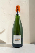 Botella de cava Wellnex Mestres Lassemblatge 13-14-16 con etiqueta blanca y cápsula naranja sobre fondo neutro