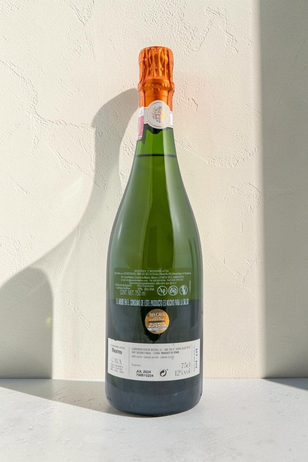 Botella de cava Wellnex Mestres Lassemblatge 13-14-16 con etiqueta informativa y cápsula naranja sobre fondo neutro.