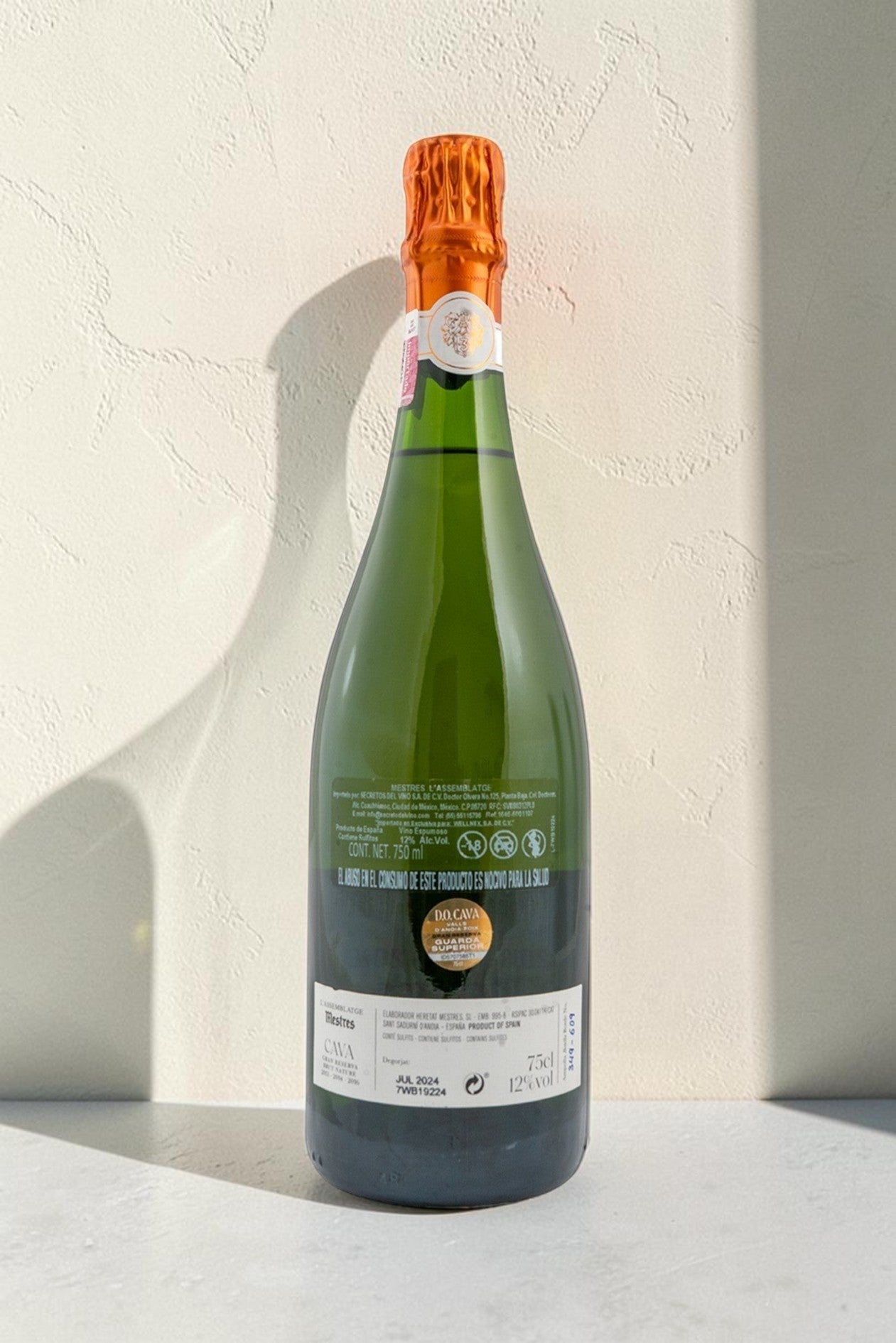 Botella de cava Wellnex Mestres Lassemblatge 13-14-16 con etiqueta informativa y cápsula naranja sobre fondo neutro.