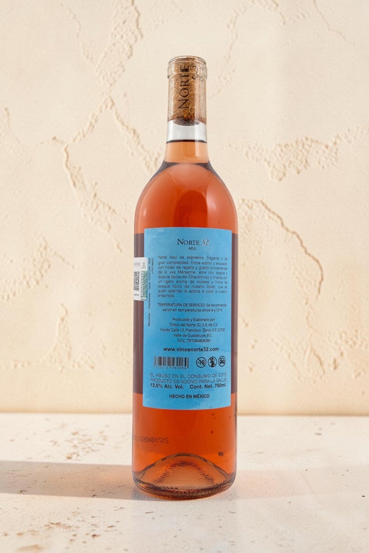 Botella de vino rosado Norte 32 Etiqueta Azul de Wellnex con etiqueta informativa sobre fondo crema