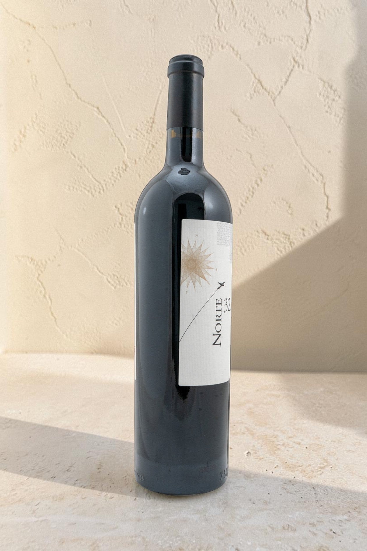 Botella de vino tinto Wellnex Norte 32 Etiqueta Blanca con etiqueta minimalista sobre fondo de piedra beige