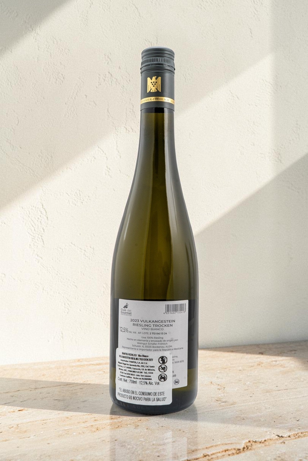 Botella de vino blanco Wellnex Schafer Frohlich Vulkangestein Riesling Trocken sobre superficie de piedra clara
