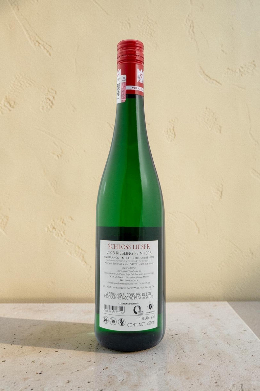Botella de vino blanco Wellnex Schloss Lieser Riesling con etiqueta trasera detallada sobre superficie de piedra