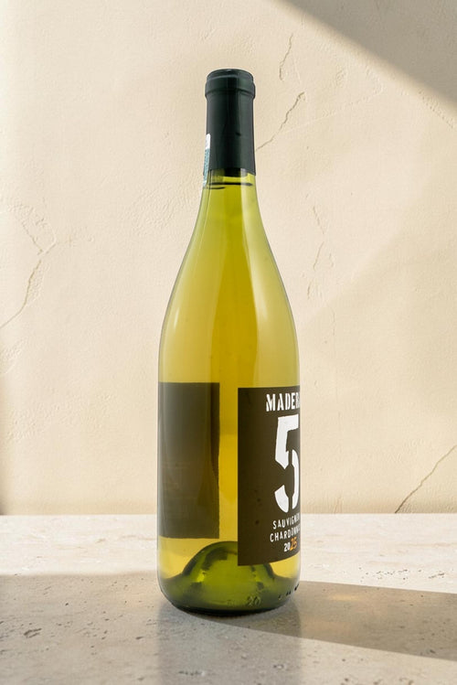 Botella de vino blanco Wellnex Sauvignon-Chardonnay de color amarillo paja brillante sobre fondo de piedra