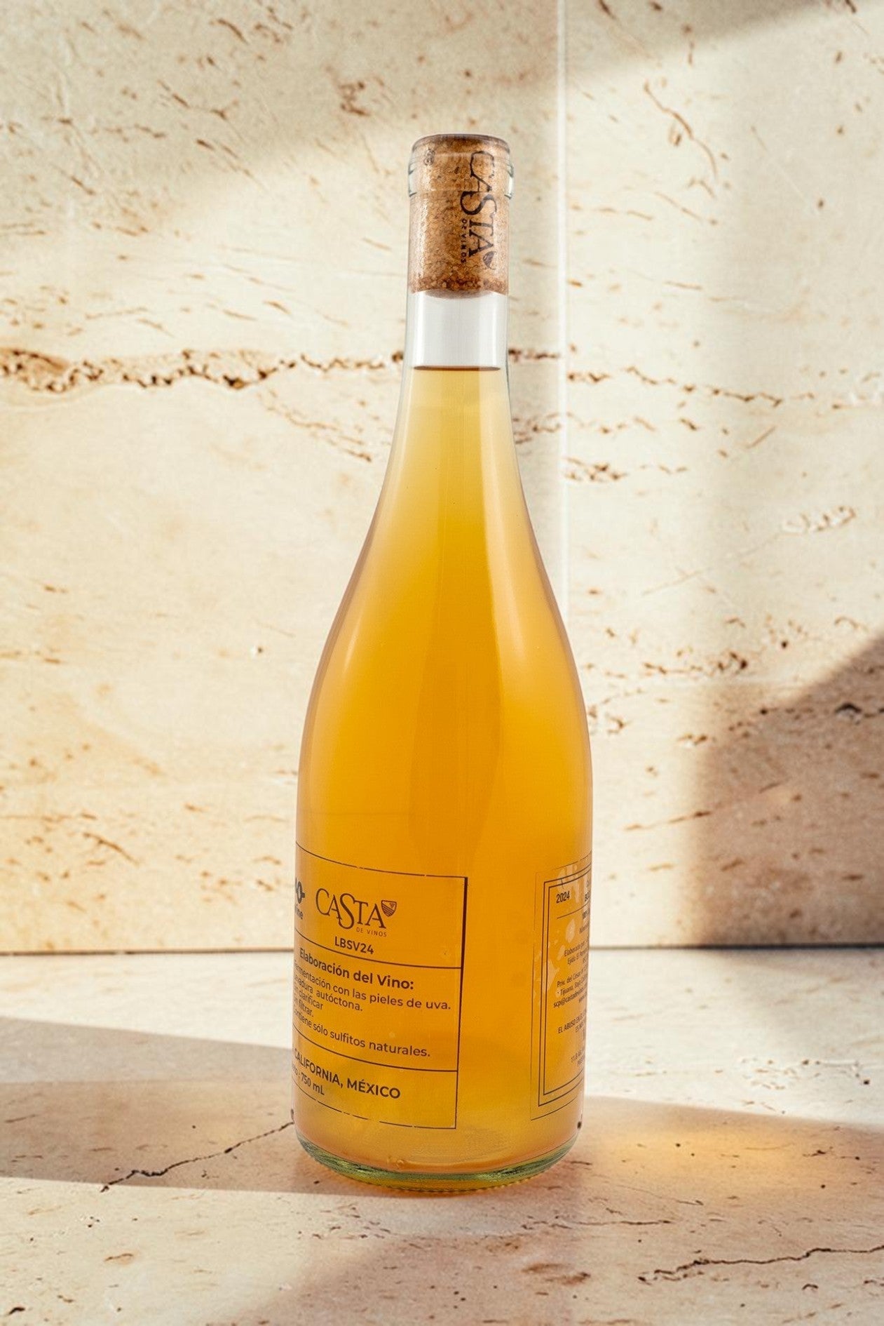 Botella de vino natural Wellnex de color amarillo ámbar turbio con etiqueta informativa sobre fondo de piedra beige