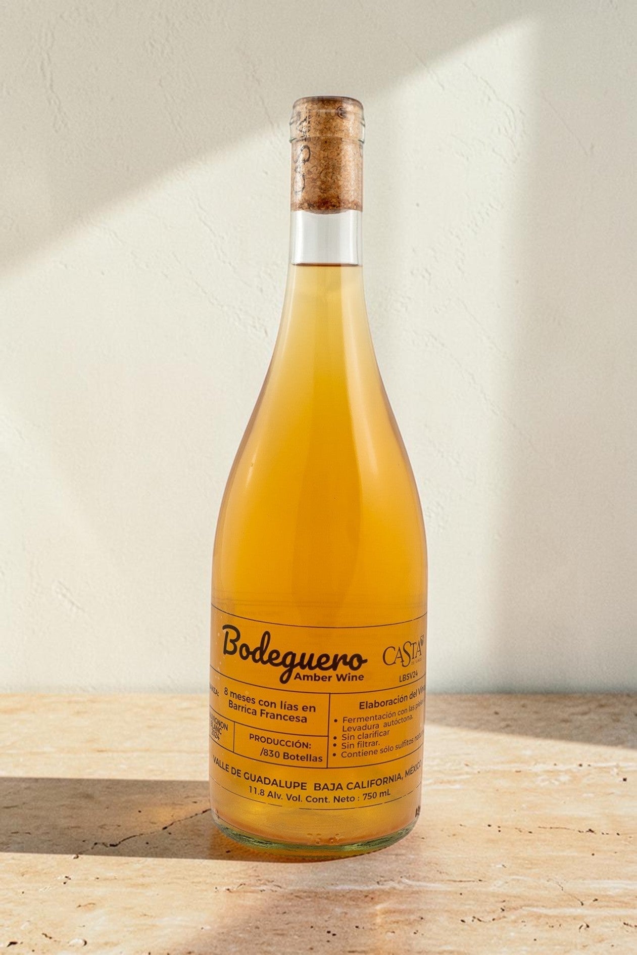 Botella de vino natural Wellnex Bodeguero color ámbar turbio con etiqueta informativa sobre fondo de piedra