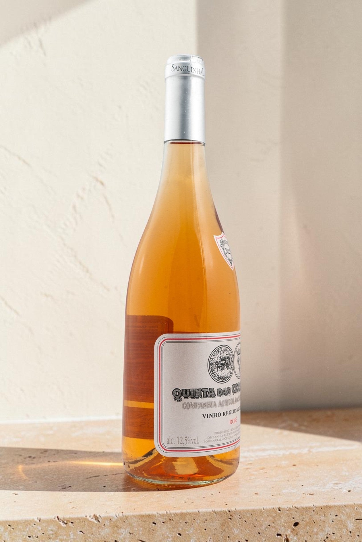 Botella de vino rosado Gran Reserva Wellnex con tonos salmón, etiqueta clásica y fondo de piedra iluminado