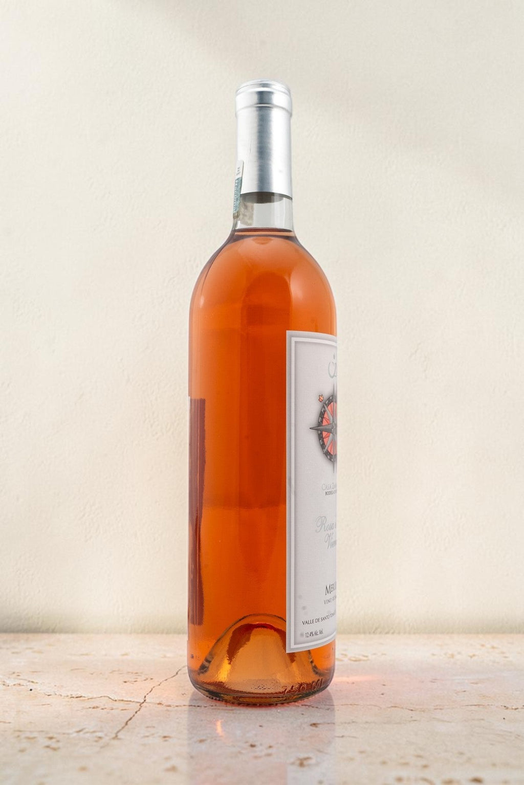 Botella de vino rosado Wellnex Rosa de Los Vientos con etiqueta de brújula sobre superficie de piedra clara