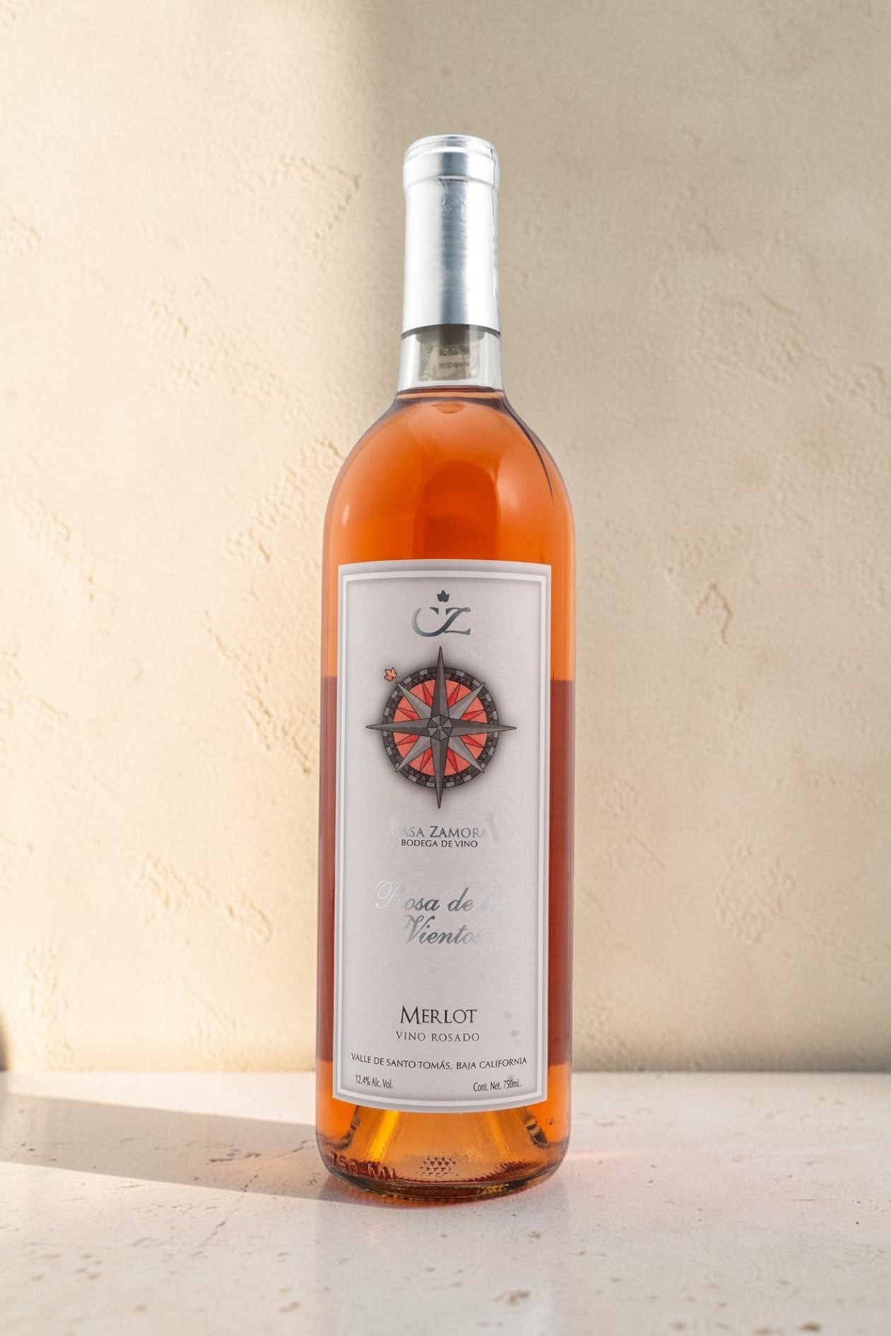 Botella de vino rosado Wellnex Rosa de Los Vientos con etiqueta de brújula sobre fondo de piedra clara