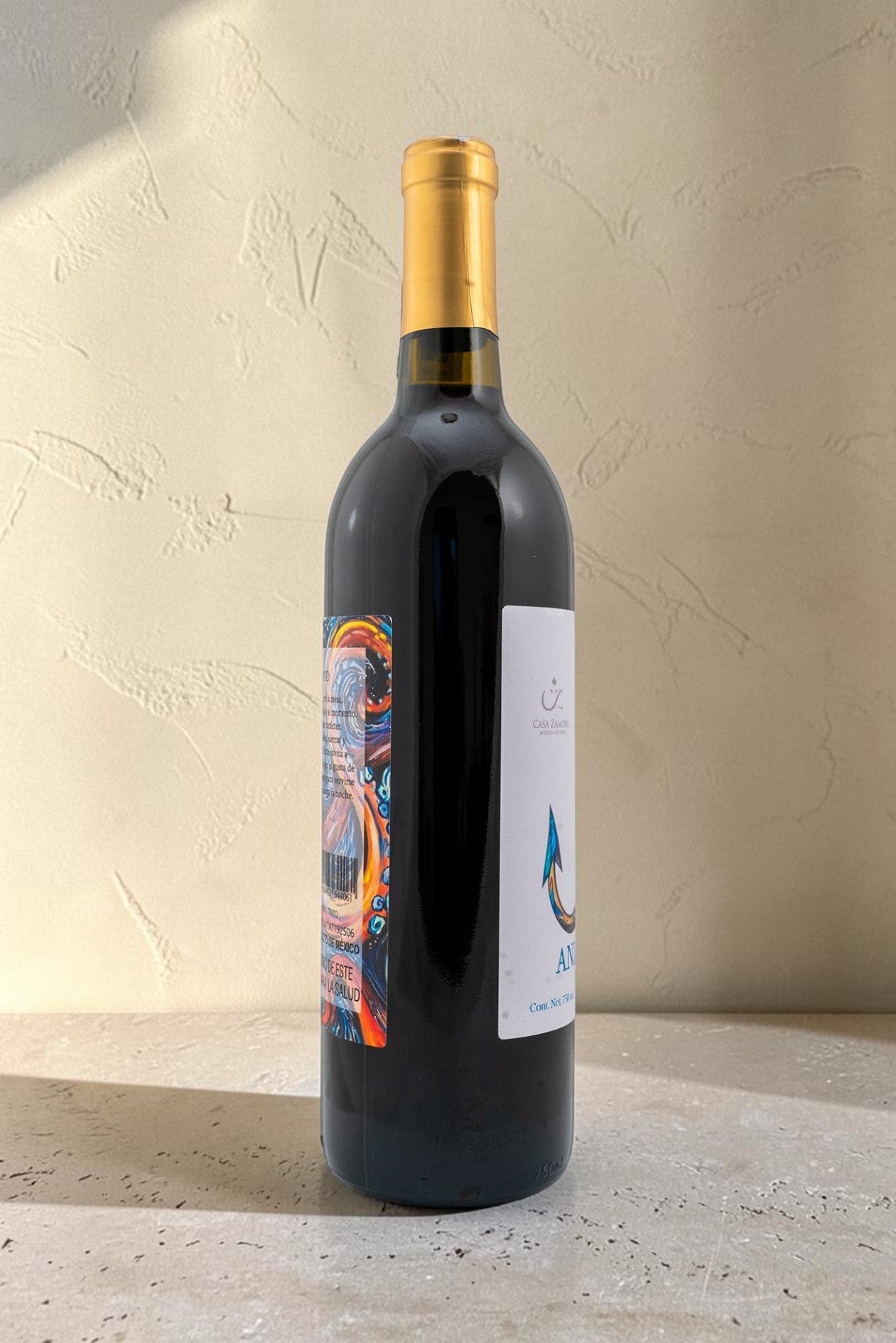 Botella de vino tinto Anzuelo de Wellnex con etiqueta colorida y cápsula dorada sobre fondo neutro