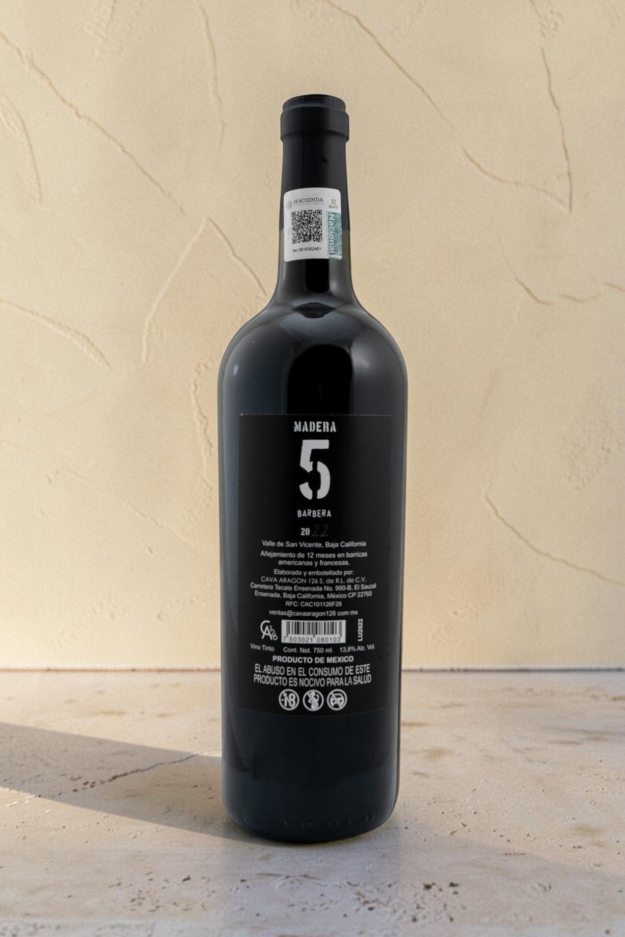 Botella de vino tinto Wellnex Barbera Madera 5 con etiqueta negra detallada sobre fondo beige