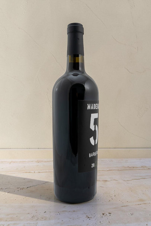 Botella de vino tinto Wellnex Barbera de color rojo rubí con etiqueta negra moderna sobre fondo neutro