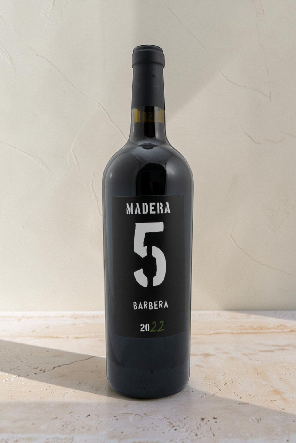 Botella de vino tinto Barbera Wellnex de color rojo rubí, con etiqueta negra y diseño minimalista sobre fondo claro.