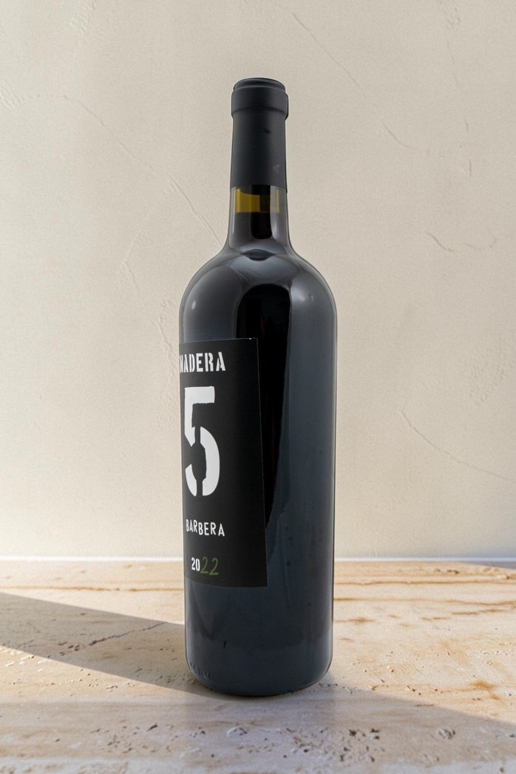 Botella de vino tinto Wellnex Barbera con etiqueta negra, diseño minimalista y reflejos brillantes sobre superficie clara