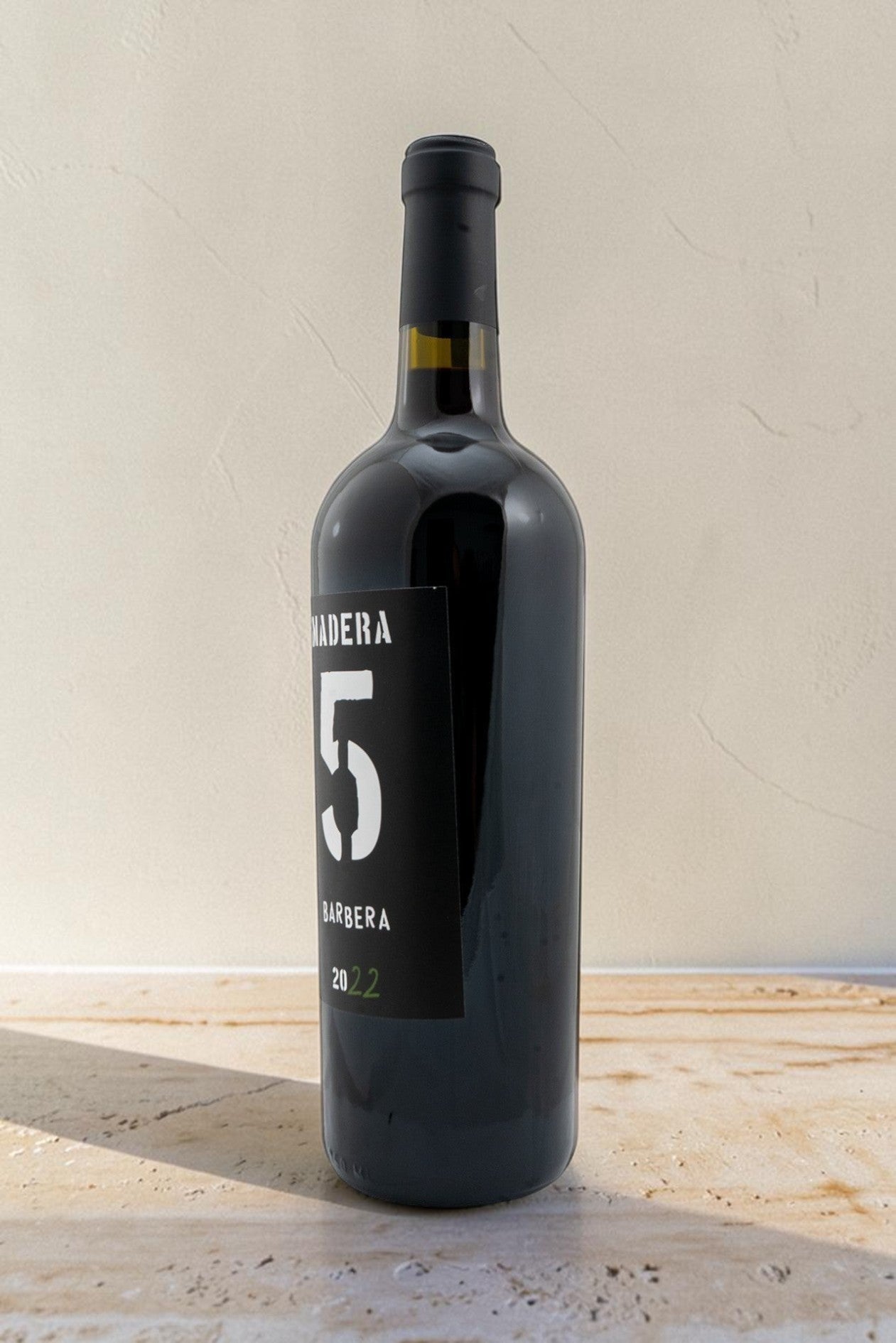 Botella de vino tinto Wellnex Barbera con etiqueta negra, diseño minimalista y reflejos brillantes sobre superficie clara