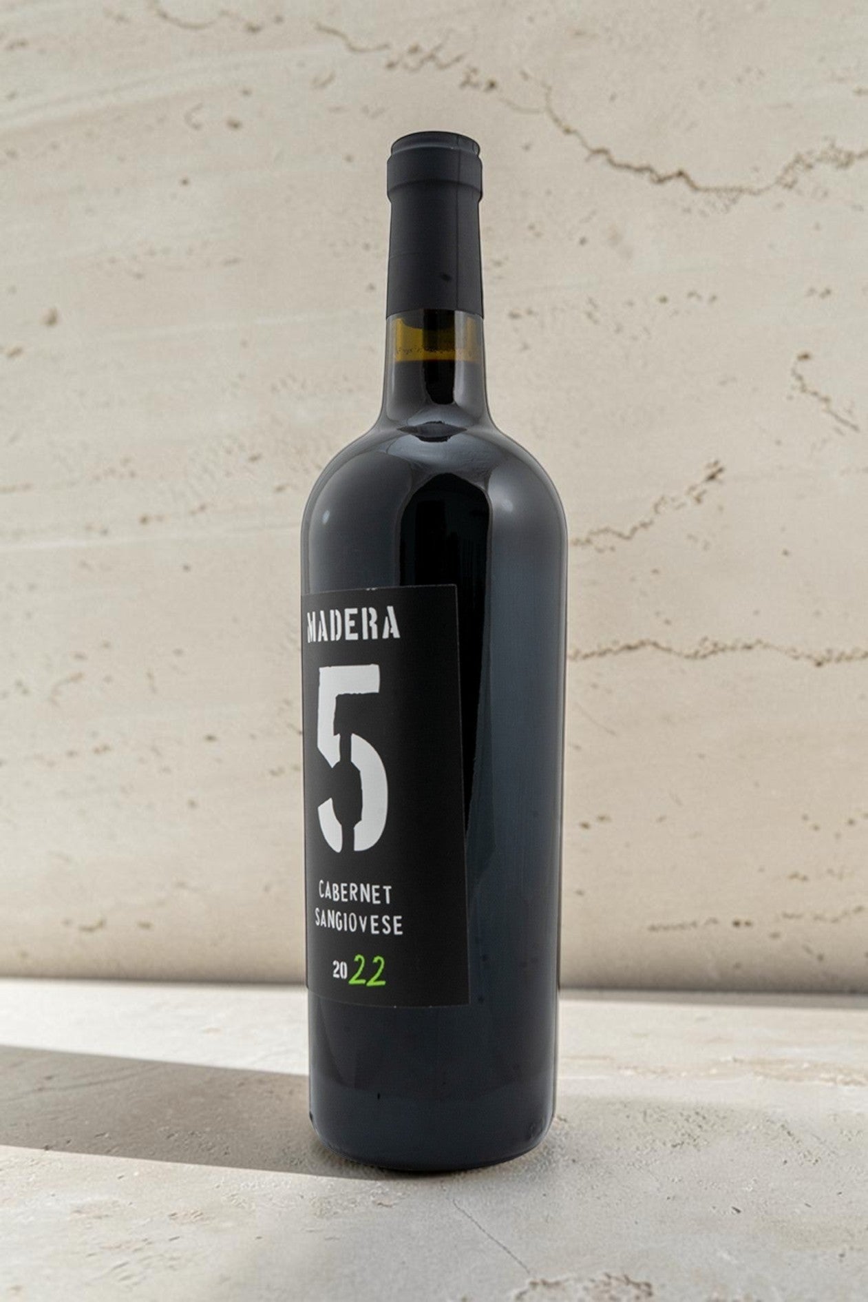 Botella de vino tinto Wellnex Cabernet Sangiovese 2022 con etiqueta negra moderna sobre fondo de piedra clara