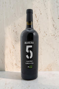 Botella de vino tinto Wellnex Madera 5 Cabernet Sangiovese 2022 con etiqueta negra moderna sobre fondo de piedra