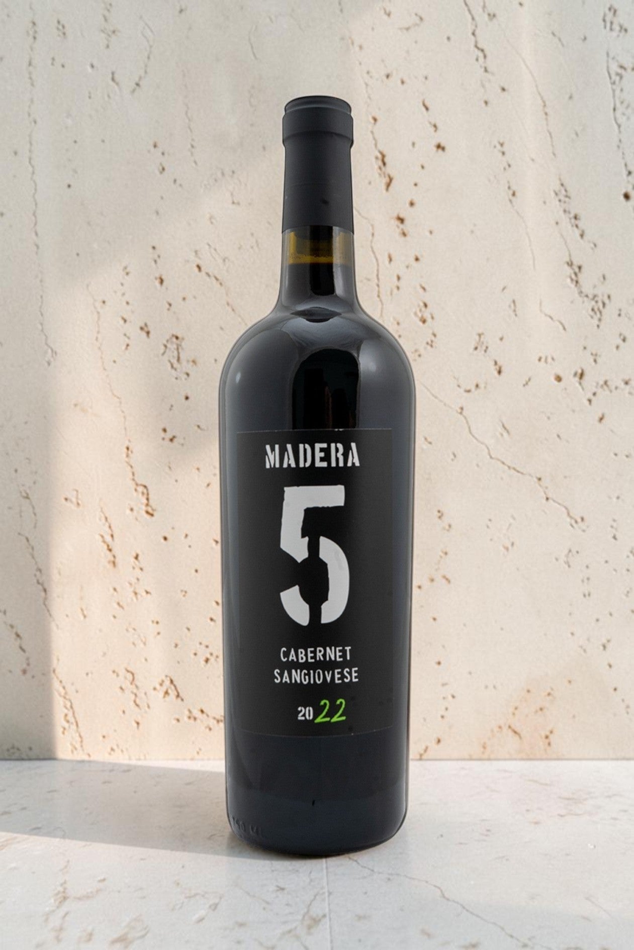Botella de vino tinto Wellnex Madera 5 Cabernet Sangiovese 2022 con etiqueta negra moderna sobre fondo de piedra
