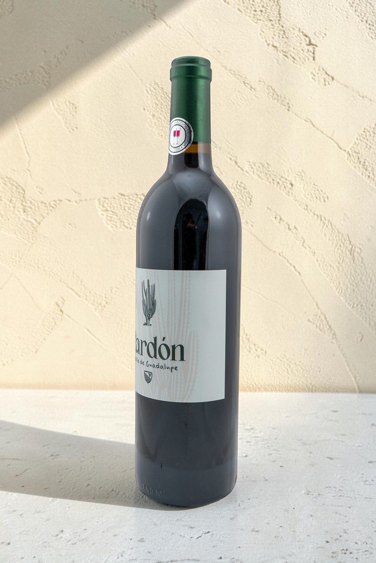 Botella de vino tinto Wellnex Cardon con etiqueta minimalista y cápsula verde sobre fondo texturizado claro