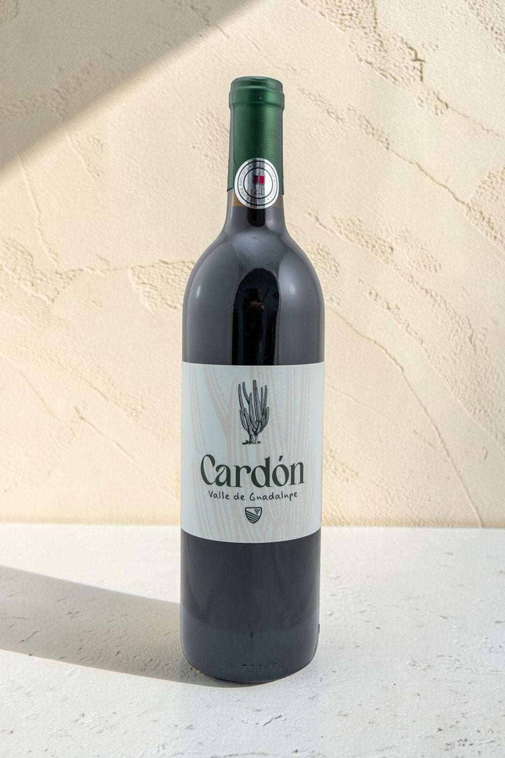 Botella de vino tinto Wellnex Cardon con etiqueta de diseño de cactus sobre fondo texturizado claro