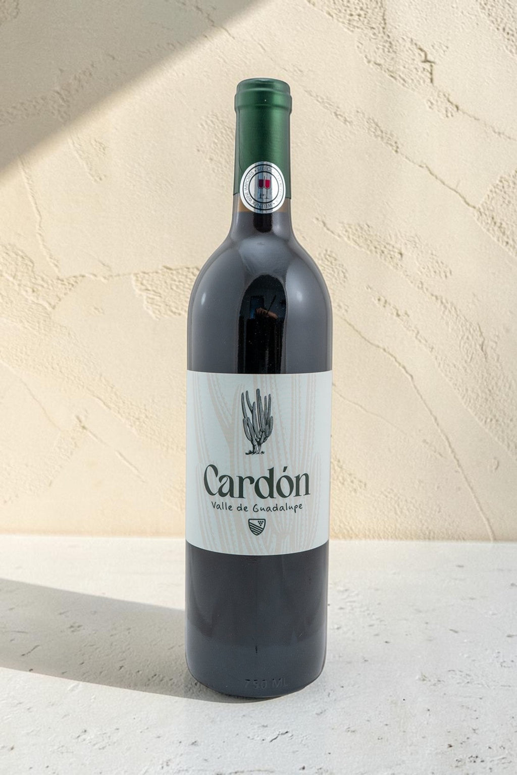 Botella de vino tinto Wellnex Cardon con etiqueta minimalista sobre fondo texturizado color crema