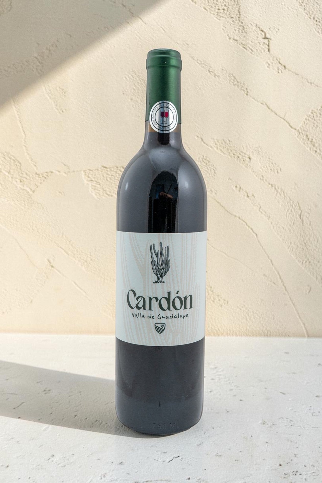 Botella de vino tinto Wellnex Cardon con etiqueta minimalista sobre fondo texturizado color crema