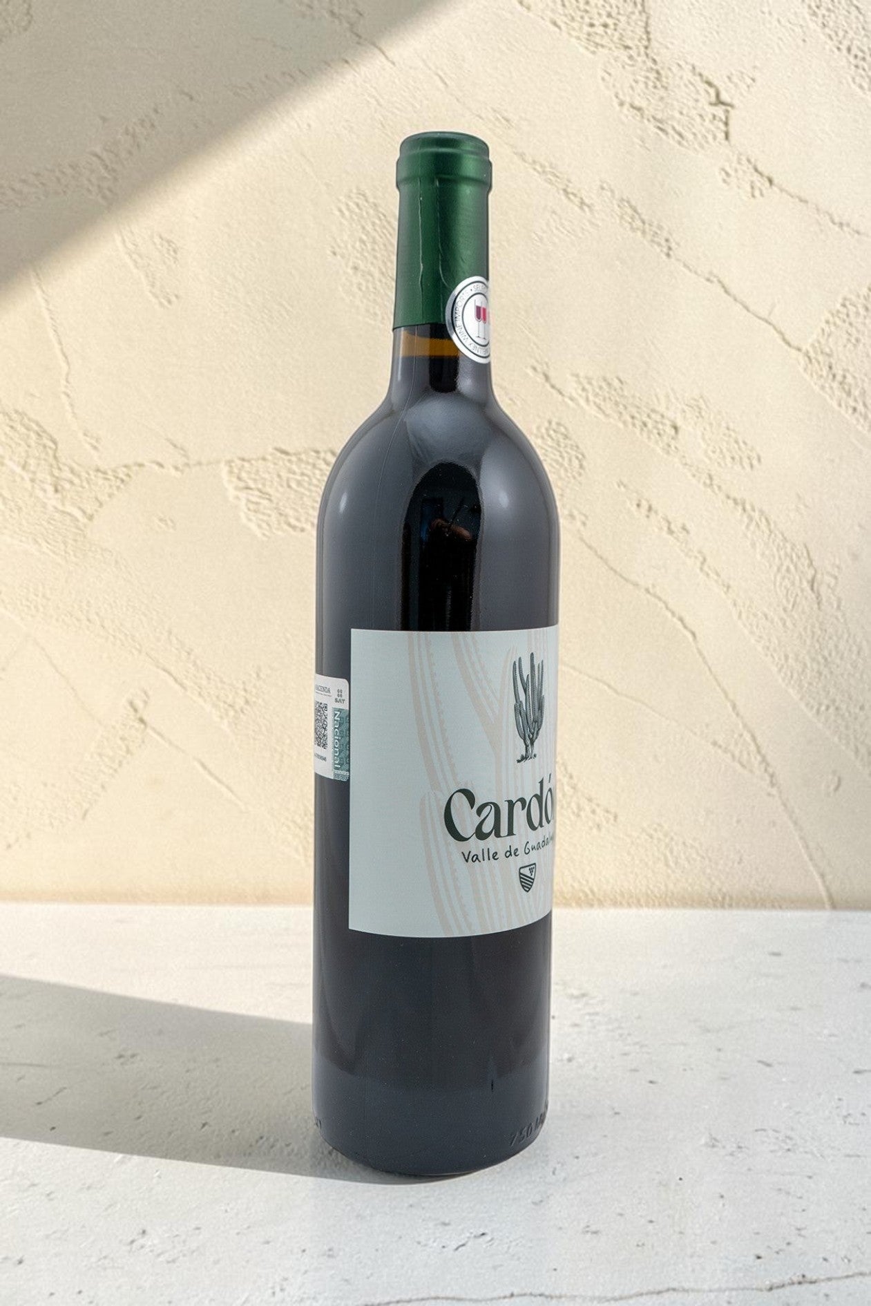Botella de vino tinto Cardon de Wellnex con etiqueta elegante sobre fondo texturizado claro