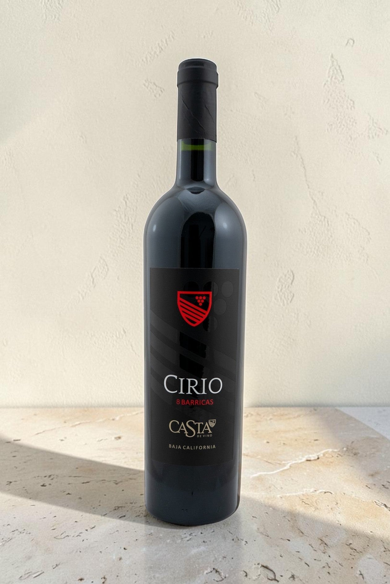 Botella de vino tinto Cirio de Wellnex con etiqueta negra y escudo rojo sobre superficie de piedra clara