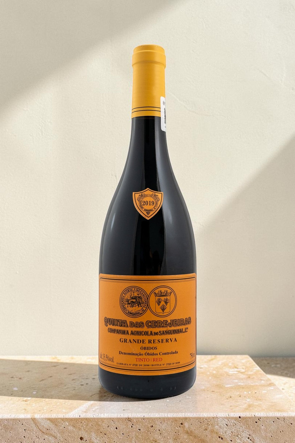 Botella de vino tinto Wellnex Gran Reserva con etiqueta naranja y cápsula amarilla sobre superficie de piedra